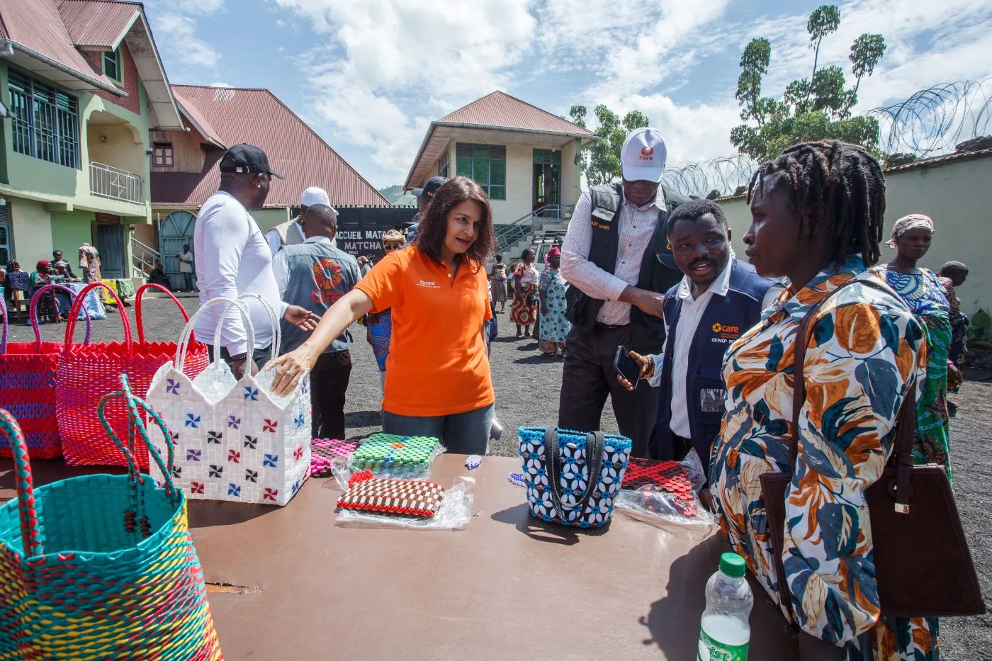 Village Savings and Loan Association (VSLA) members showcase handmade clothes, baskets, and local produce on display while CARE staff wearing branded vests and t-shirts talk with them.