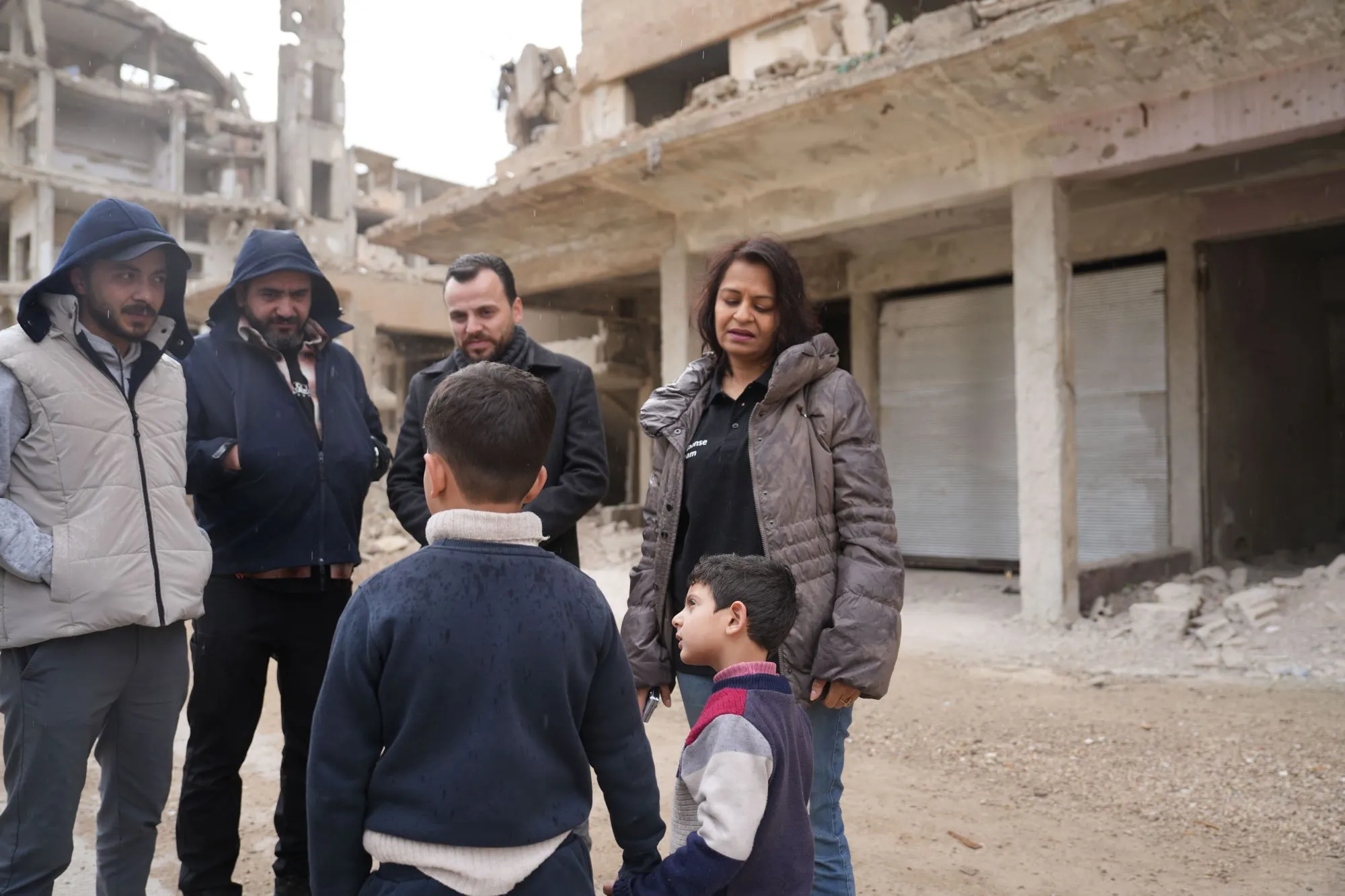 Humanitarian workers look on as two children, their faces devoid of emotion, stand amidst the devastation.