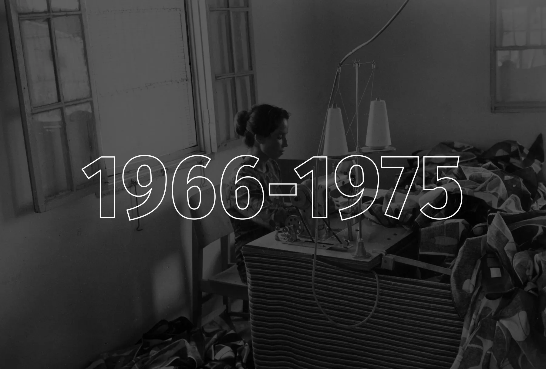 A woman sits at a desk and sews on a sewing machine.