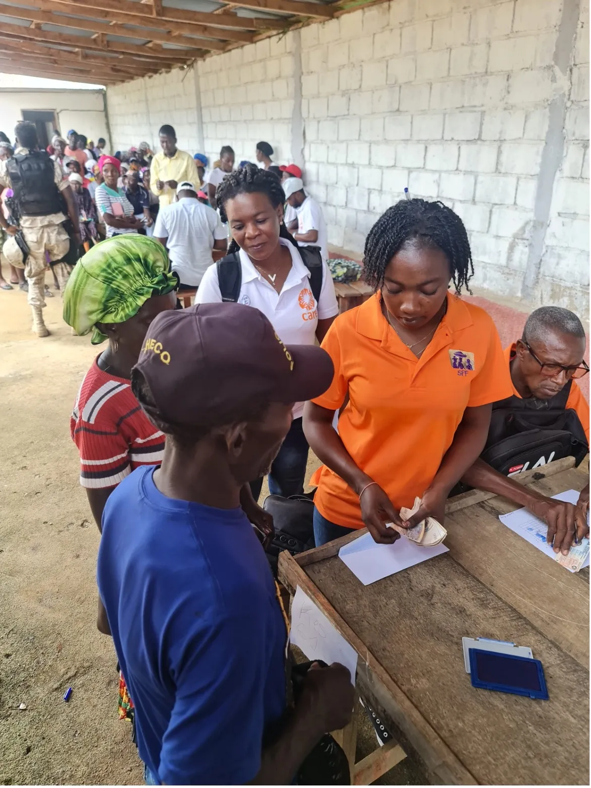 Several people gather around a woman in orange shirt counting out cash.