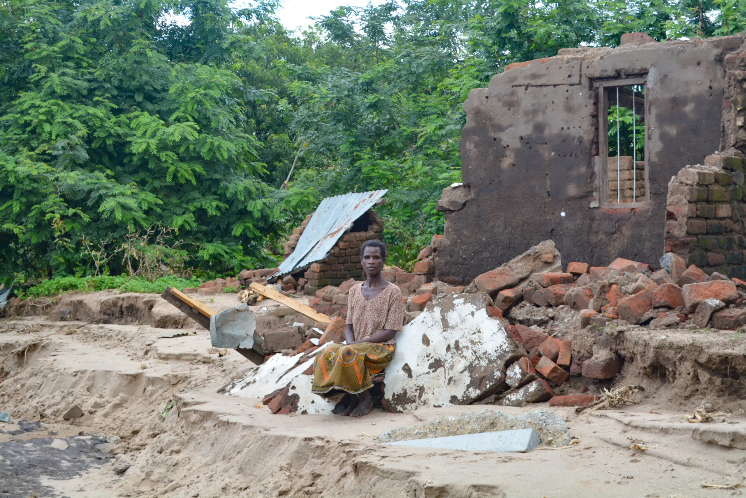 A woman sits alone amidst the rubble of a destroyed home.