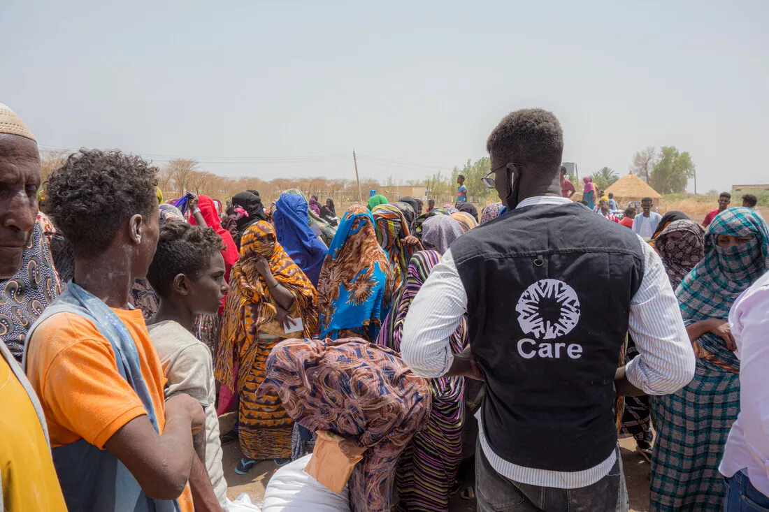 A man wearing a CARE vest talks with a large group of people.