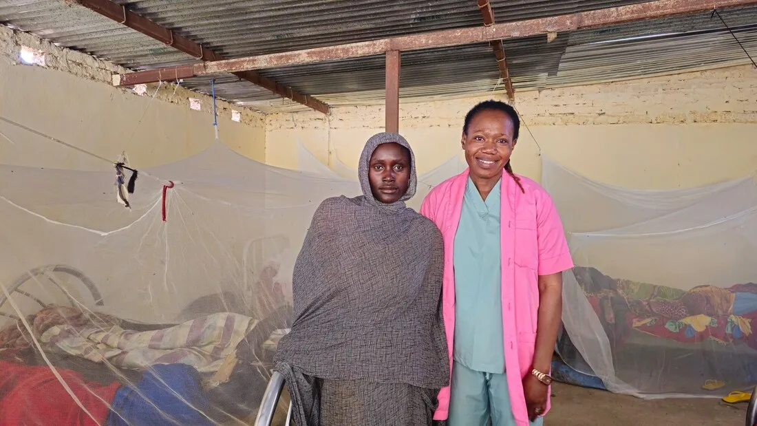 Two women stand side by side in front of mosquito-netted beds at a CARE-sponsored clinic in Chad.