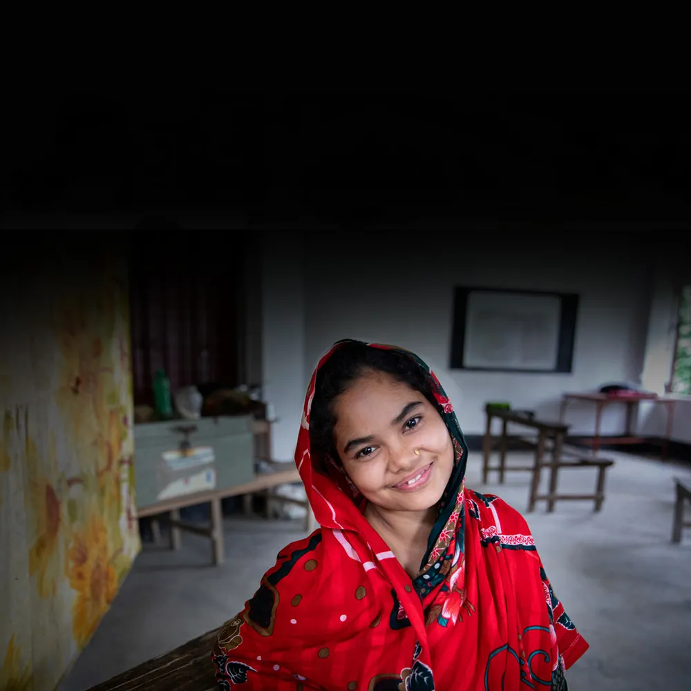 A young girl smiles while sitting in a classroom.